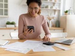Female business owner sitting at kitchen table holding phone and looking over financial documents.
